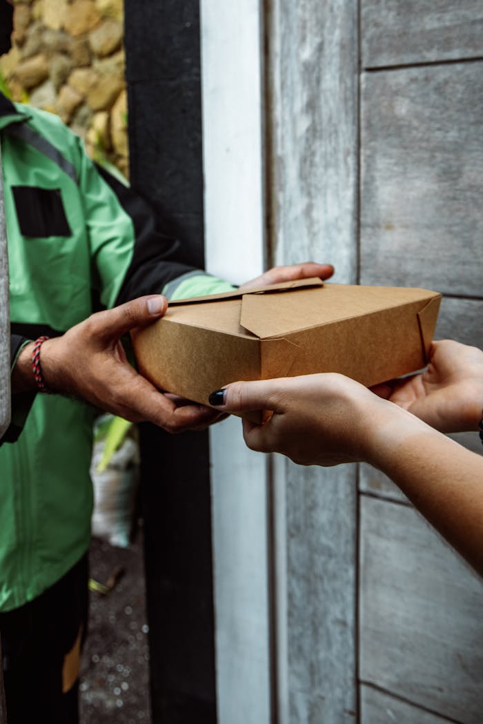 Close-up of hands exchanging a craft paper package outdoors, symbolizing delivery service.