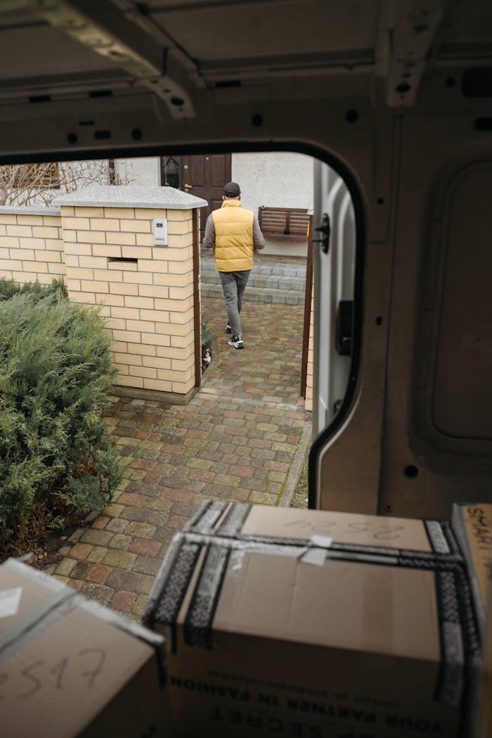 Courier in yellow vest delivering packages to a house, viewed from inside van.