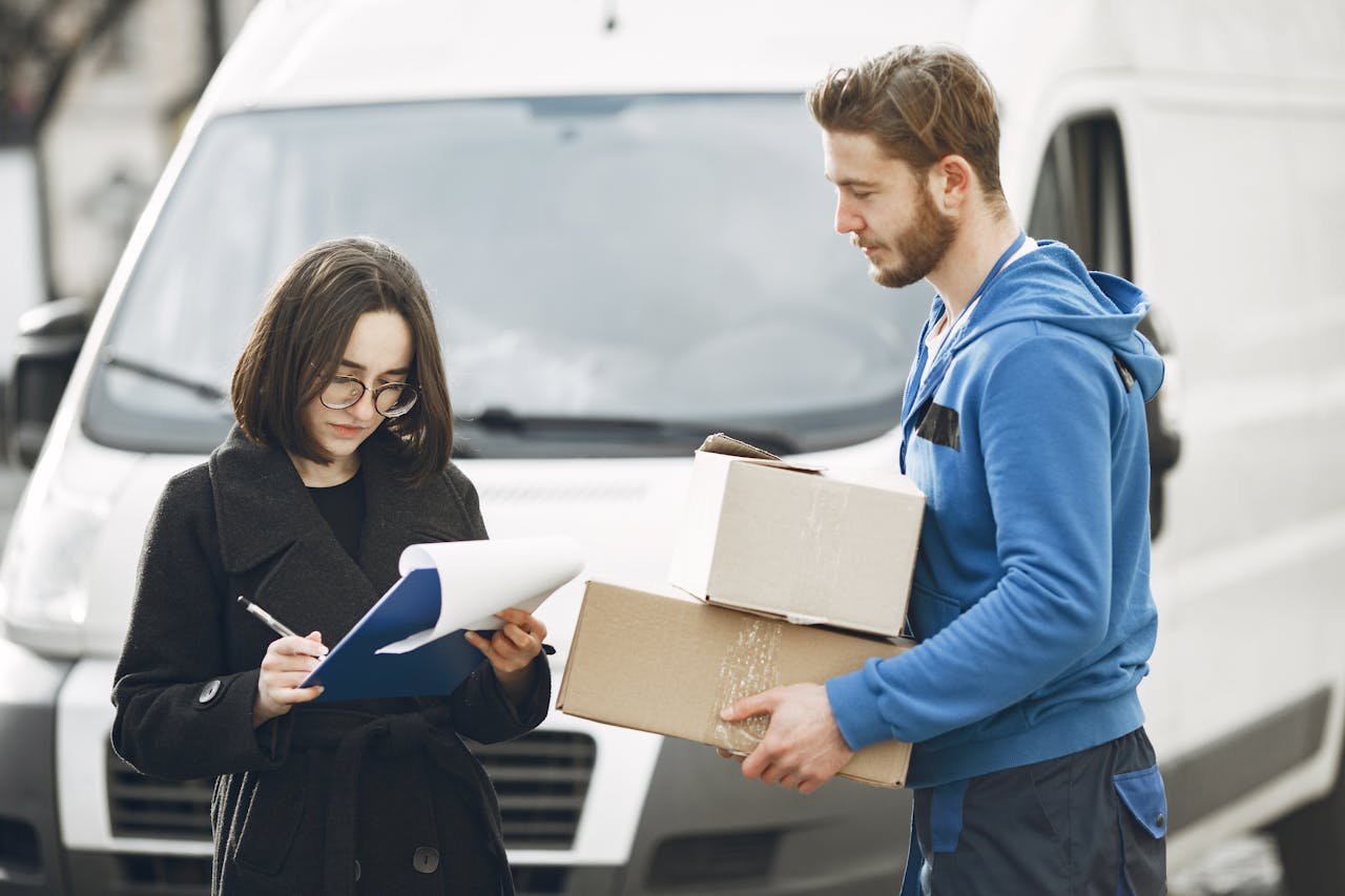 why-choose-us A courier in blue hands packages to a woman signing documents in front of a delivery van.